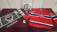 Full view of lot showing Montreal Canadiens jersey with number 33, framed hockey card, and hockey-themed cloth banner.