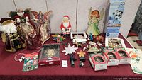 Full table view with various vintage Christmas decorations including tree toppers, boxed ornaments, light-up star, and framed decors.