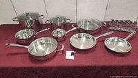 Full set of stainless steel pots, pans and spice jars arranged on table with red cloth