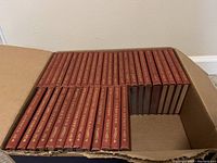 Cardboard box containing 36 red hardcover volumes arranged spine-up