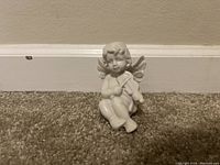 Photo showing the angel figurine holding a violin, placed against a beige wall on brown carpet.