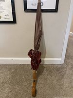 Closed umbrella leaning against the wall showing wooden handle and folded fabric