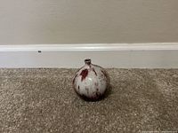 Front view of small rounded ceramic vase with marbled red and white finish displayed on carpet.