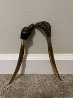 Full view of the pair of letter openers placed against a wall, showing the eagle and dog head handles and curved blades.