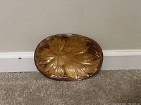 Front view of oval wooden plate with carved leaf design and glossy finish.