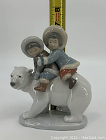 Front view of LLadro porcelain figurine showing two children riding polar bear with measuring tape showing height approx 7.5 inches