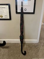 Umbrella closed with visible curved handle and plaid fabric wrapped around.