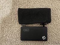 Photo showing the INIU phone bank charger and its black mesh carrying pouch placed on a carpet surface.