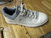 Side profile of white sneaker showing leather upper, lace eyelets, midsole, and logo on side.