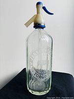 Full view of the vintage clear glass NU Jersey Creme seltzer bottle with blue and cream spout, showing whole bottle and neck.
