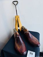 Pair of antique wooden shoe forms with metal handles and adjustment knobs shown together on black surface.