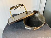 Cast iron meat press with coil spring handle and cast iron baking dish with curved handles shown side by side.