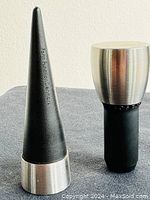 Front view of two Erik Bagger Rosendahl Grand Cru Form Function wine stoppers, one pointed and one rounded top, placed on grey fabric background.
