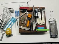 Photo displaying the entire lot including cutting board, Victorinox knife, measuring spoons, fondue forks, wine stopper, and other kitchen tools.
