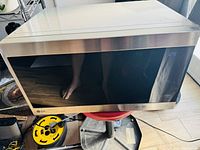 Full front view of LG microwave oven on wooden floor, showing stainless steel edges and dark glass door reflecting surroundings and person taking photo.
