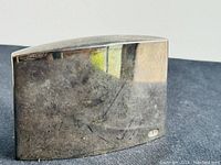 Curved rectangular silver salt and pepper shaker with reflective surface and signs of wear.