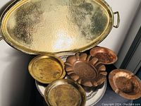Overall view of all trays and dishes: brass oval tray, sterling silver dish, brass plates, copper dishes