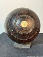 Close up of the antique Thomas Taylor wooden lawn bowling ball featuring an inlaid brass medallion marked 'B' with visible wear and carved circle details on the surface.