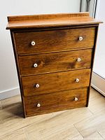 Front view of a wooden four-drawer pine cabinet with white ceramic handles.