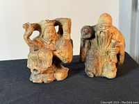 Two carved petrified wood sculptures of an elderly man with staff and woman seated, displayed on black fabric.