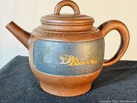 Side view showing one painted tiger on dark blue background along with the spout and handle of the reddish clay teapot.
