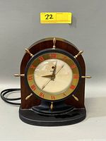 Front view of vintage Telechron electric mantle clock with nautical wheel style brass accents, red Roman numerals, wooden and black base with glass clock face.