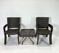 Two black steel mesh stacking armchairs flanking a matching black steel mesh outdoor table with curved tubular legs.