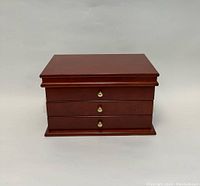 Front view of closed wooden jewelry box with three drawers and round metal knobs.