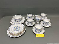 Full view of entire tea set showing cups, saucers, creamer, sugar bowl, bread and square plates on gray background.