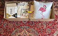 Box with folded linens and flamingo throw pillow inside, showing all items included in the lot.