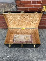 Open vintage flat top trunk showing plywood interior and floral hook rug inside.