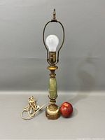 Front view of the green onyx and brass lamp with light bulb and cord next to an apple for scale.