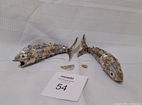 Two fish-shaped vintage bottle openers displayed side by side with loose fin parts front and center; damage circled in photos