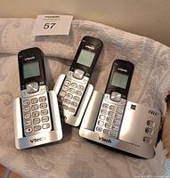 Three VTech cordless handsets with one base station shown together on blanket surface.