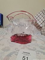 Full front view of artistic glass vase with wavy top and red base on fabric surface