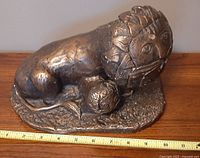 Side view of the vintage Austin Productions metal lion sculpture showing the larger lion with textured mane and smaller lion figure beside it on an oval textured base. A measuring tape is positioned in front showing the length.