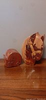 Photo showing the carved wooden horse and cat locking treasure boxes side by side on a wooden surface against a plain wall background.