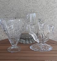 Set of three crystal and glass items on wooden surface: fan-shaped vase, large ice bucket, and three-arm candelabra.