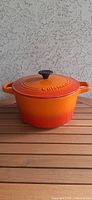 Front view of orange ombre cast iron casserole with lid on wooden surface in front of textured grey wall.