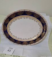 Oval antique plate laid flat showing full face with blue and gold intricate pattern on white ceramic.