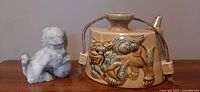 Front view of carved marble foo dog figurine next to ceramic foo dog saki flask, showing textures and details