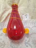 Full front view of the red glass vase with orange swirl handles and bands on neck and body.