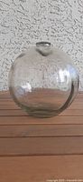 Front view of clear, blown glass fishing float with visible texture and reflections. Spherical shape with a small lip opening at the top.