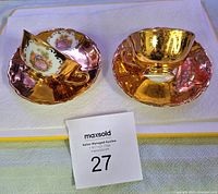 Two gold miniature tea cups with matching saucers side by side on a white surface