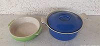 Two enameled cast iron dishes: green shallow dish on left, blue casserole with lid on right
