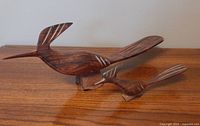 Angled side view of both carved ironwood roadrunner figures, showing wood grain and carved wing details.