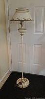 Full view of cream colored toleware floor lamp with decorated lampshade and round pedestal base.