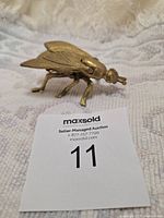 Photo showing the metal fly sculpture from the side, highlighting the brass look and shape.