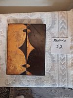 Front view of the Nexus tile showing abstract brown and gold design on a rectangular tile with visible wear and chips.