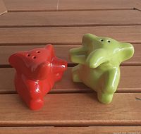 Red and green ceramic elephant salt and pepper shakers shown on wooden surface from front angle.